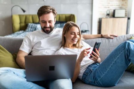 hermosa-joven-pareja-relajandose-sofa-casa-usando-computadora-portatil-telefono-movil.jpg